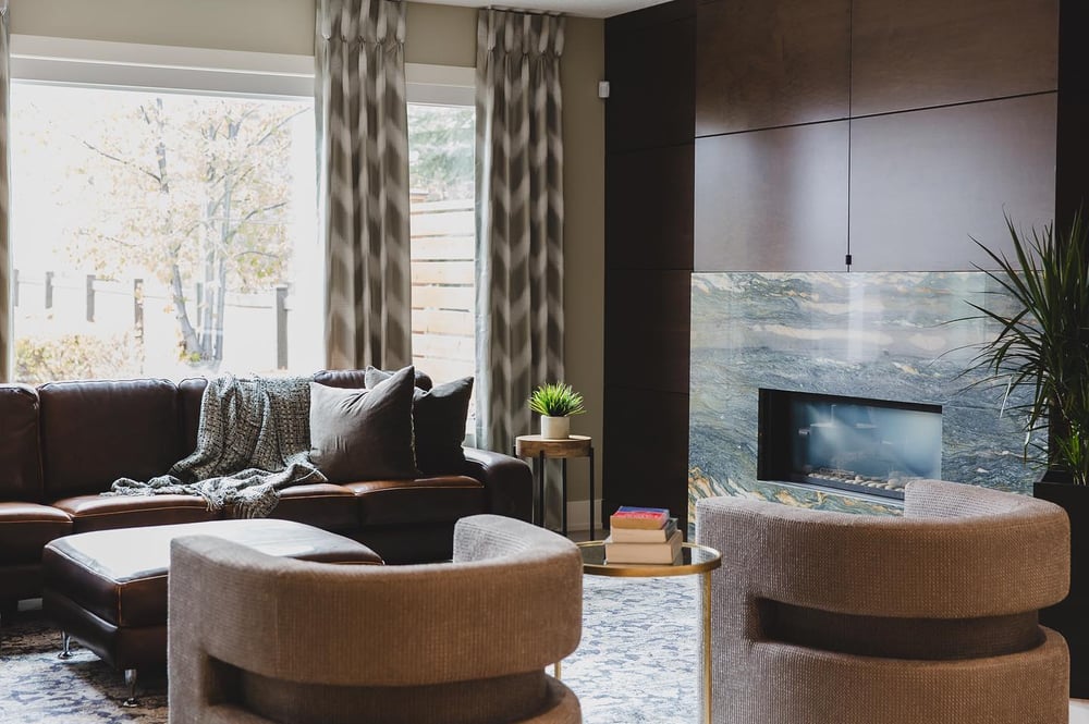 modern living room with sofa and two accent chairs and ottoman by a marble fireplace