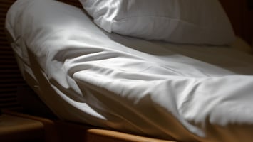 close up of the top of an adjustable bed, with part of frame showing, upright head of mattress and pillow