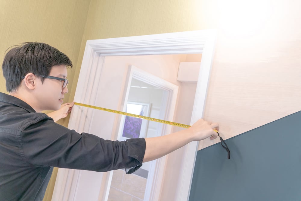 young man with glasses uses a tape measurer to measure the width of a doorway