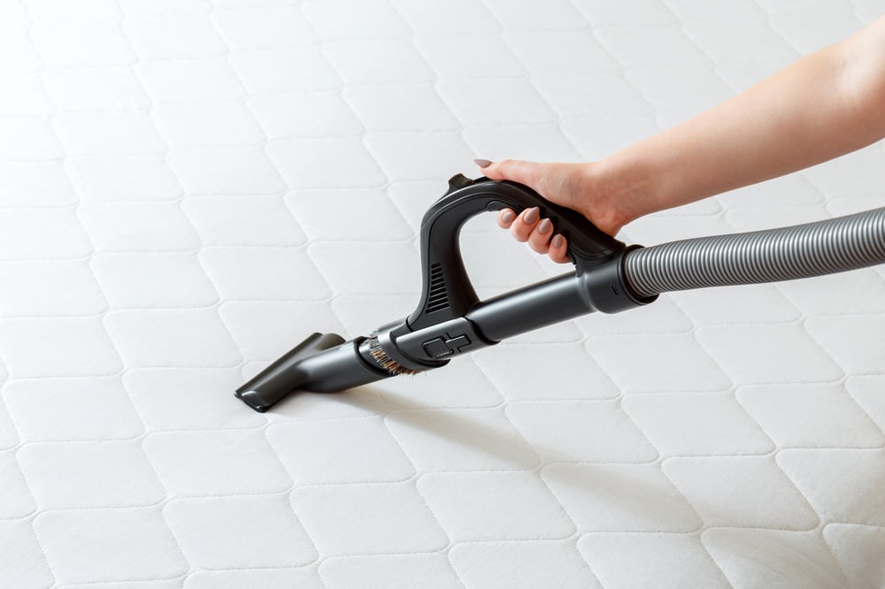 woman's hand holding a small attachment to vacuum the top of a mattress