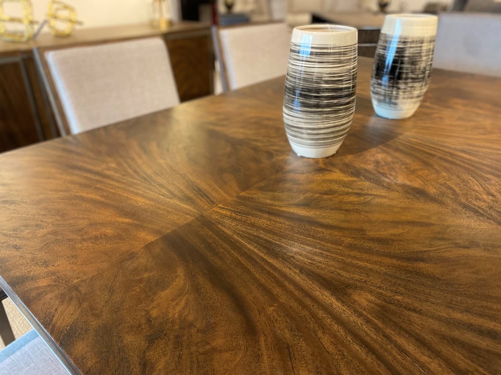 close up of a veneered wood table top with two vases on top surrounded by upholstered chairs