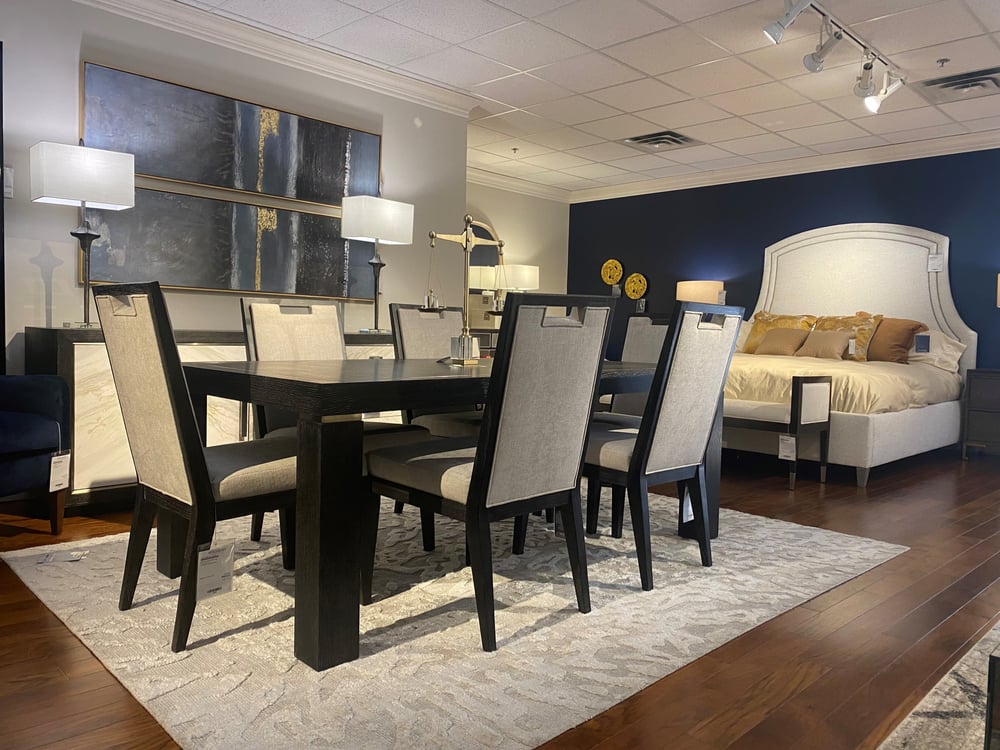 dining set with wood table and six wood and upholstered chairs, buffet behind with a picture hanging above and an upholstered bed in the background