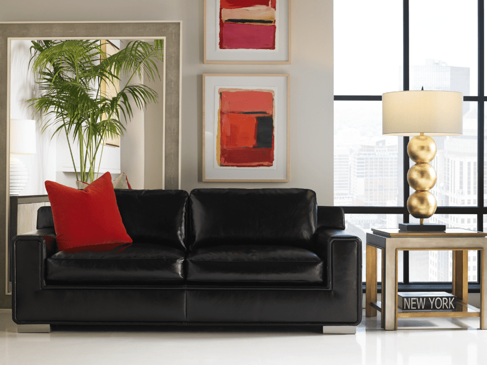 sleek leather couch with track arms and one accent pillow in front of a wall of pictures and full length mirror