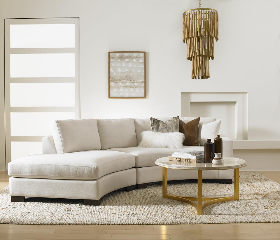 simple and neutral living room with curved sofa over an area rug with a round coffee table and a small framed picture behind the sofa