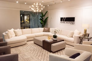 living room setting with large sectional, upholstered coffee table and four accent chairs in front of a Marcantonio Designs logo