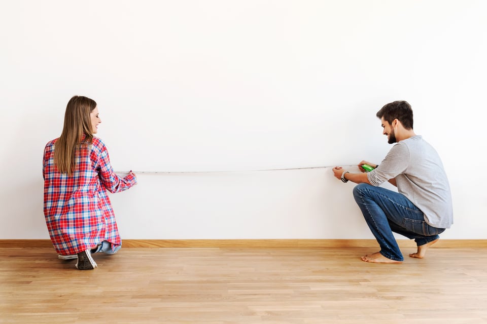 man and woman happily help eachother measure a wall 