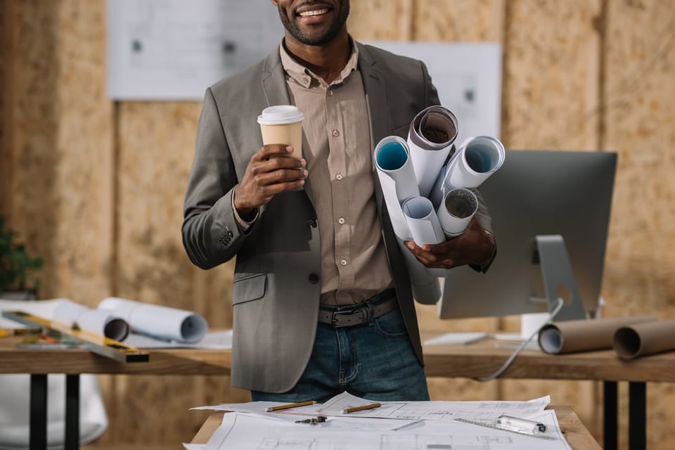 business casually dressed man holds rolled up papers and coffee on the job site