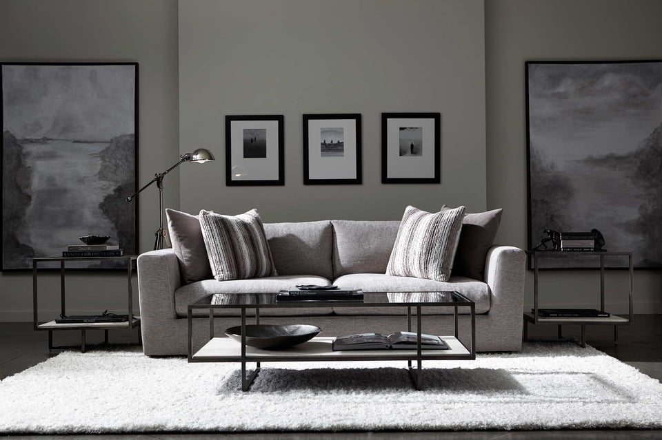 sofa with pillows behind a rectangular coffee table in front of two large pictures and three smaller ones