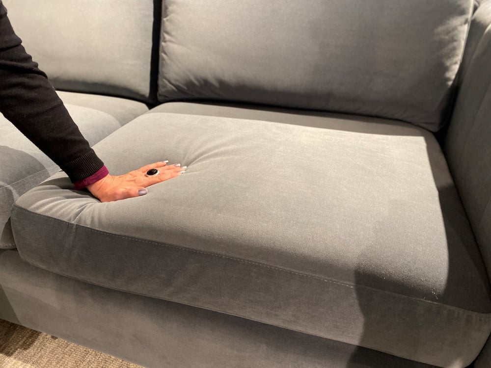 close up of a sofa seat and a woman's hand pressing down on the cushion
