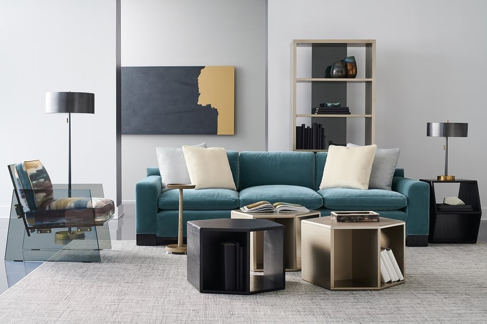 modern living room with sofa and accent chair around three hexagonal coffee tables over an area rug with a bookshelf, lamp and wall picture in the background