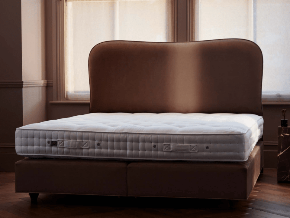 bedroom with an undressed mattress and a headboard over a divan with legs on a hardwood floor
