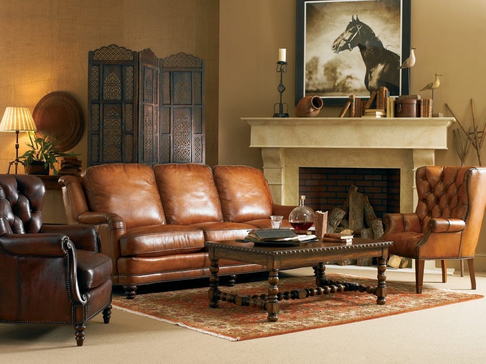 living room of leather furniture, including a sofa and two tufted chairs and a detailed wooden coffee table over an area rug in front of a fireplace