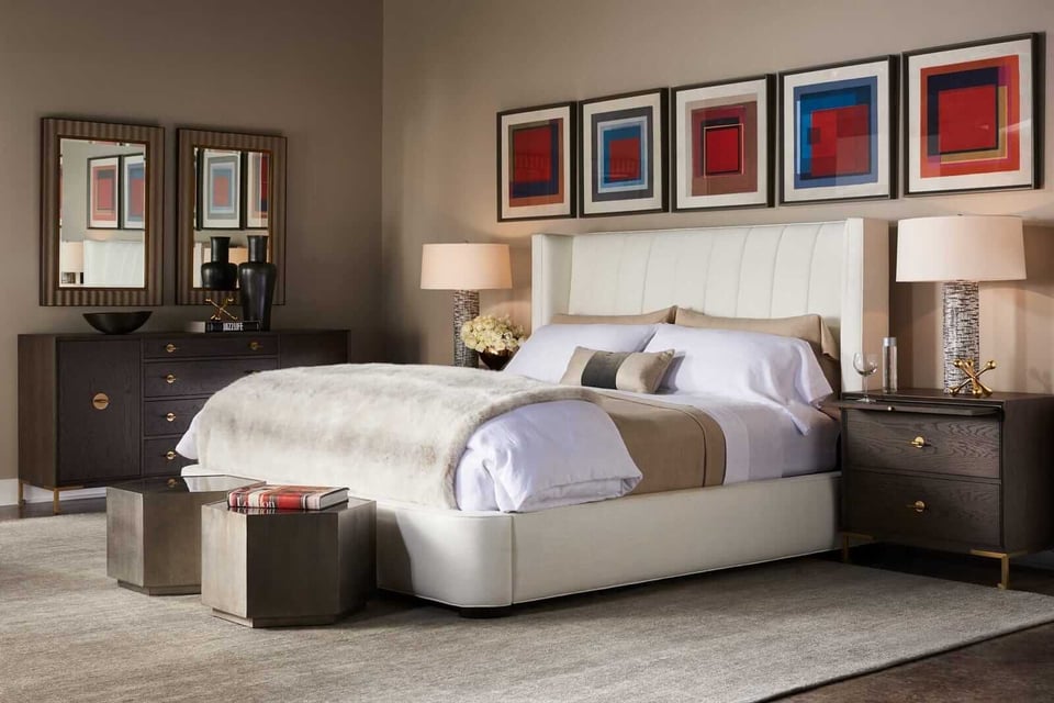 bedroom suite with upholstered bed, two nightstands with lamps, matching dresser, two hexagonal ottomans at foot of bed, and give geometric pictures above headboard