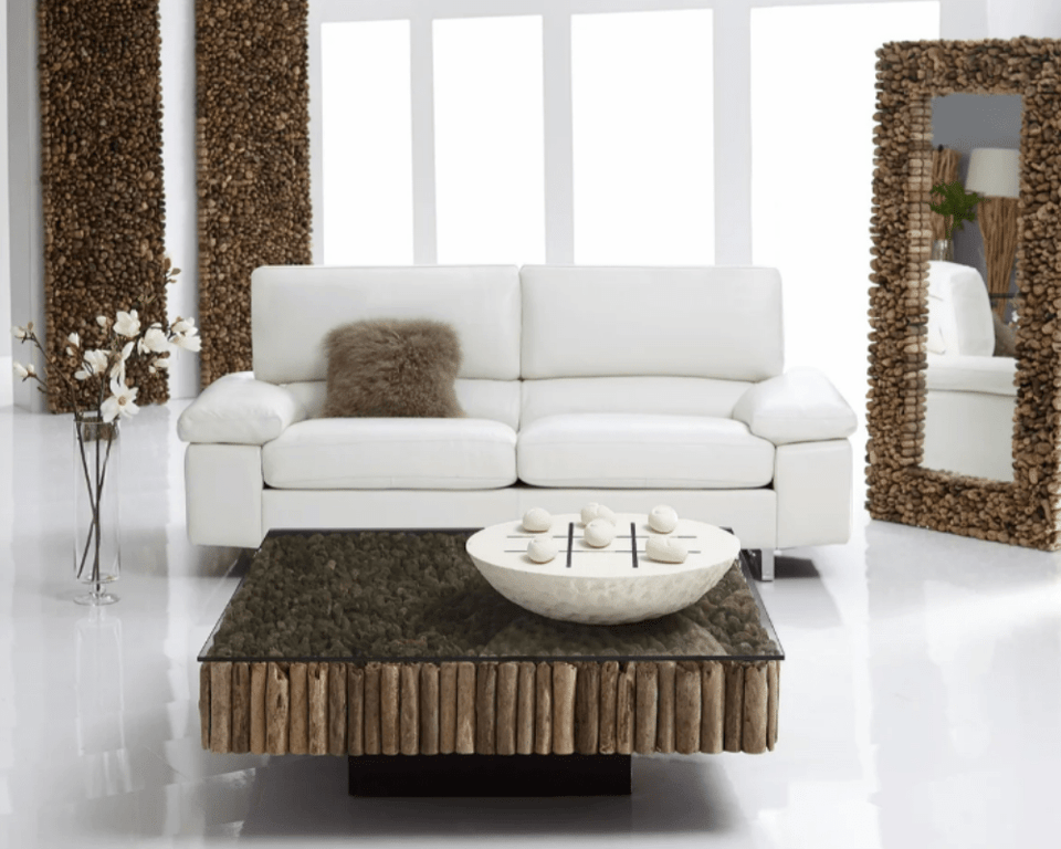 coffee table made out of narrow wooden logs and a glass top in front of a two seater sofa and a standing mirror with wooden accents