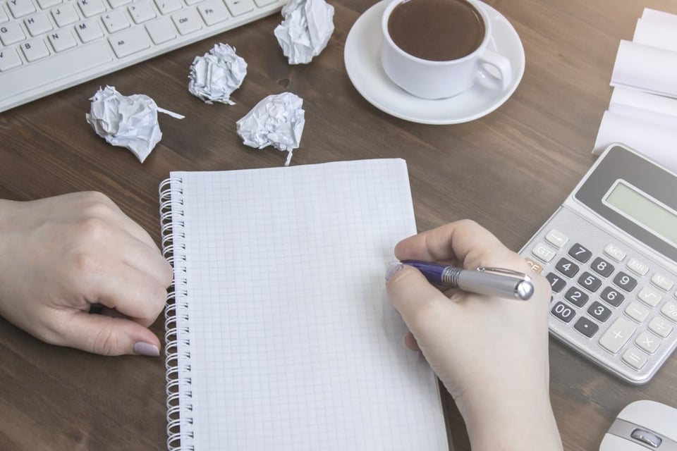 hands writing on piece of paper with cup of coffee and calculator