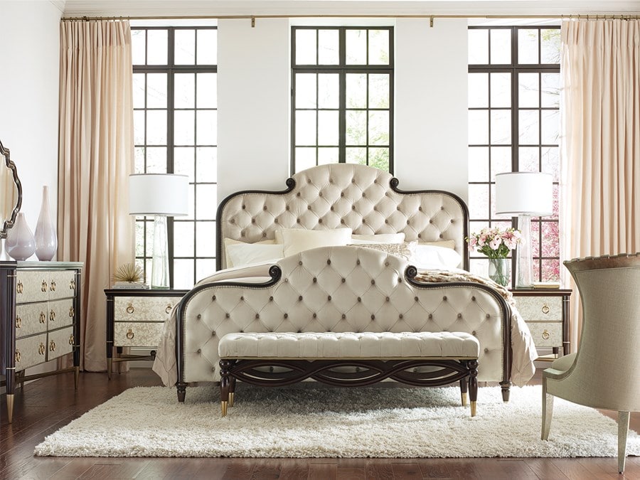 bedroom suite with traditionally tufted bed over an area rug with two nightstands, a dresser and mirror, a bench and an accent chair