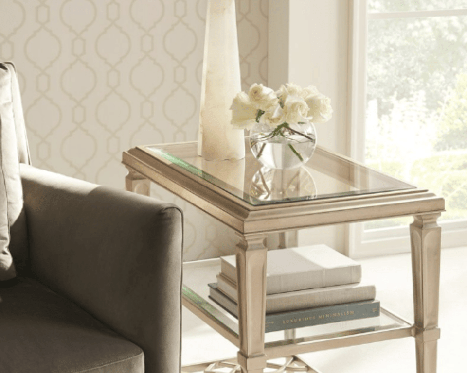 close up of end table with glass top beside a chair, with a small bouquet of flowers and an accent piece on top