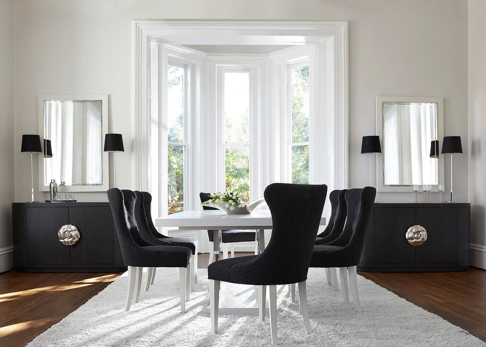 Bright dining room with six chairs around a table in front of a bay window, two hutches with two lamps on each and accent mirrors