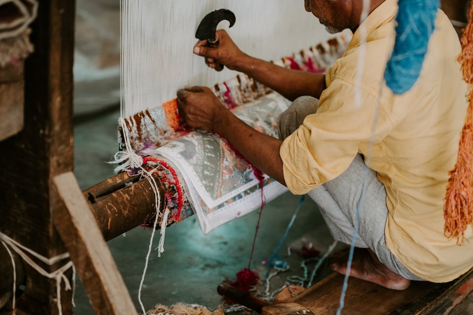 man uses tool to weave a rug on a loom