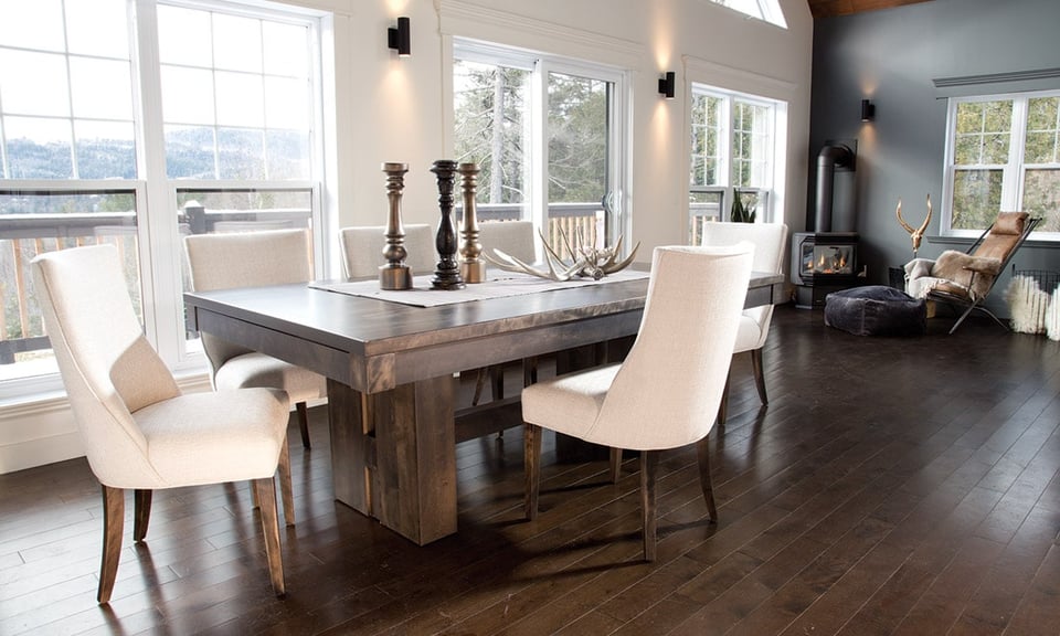 solid wood dining table with six upholstered chairs adjacent to a cozy reading nook with chair by a wood stove