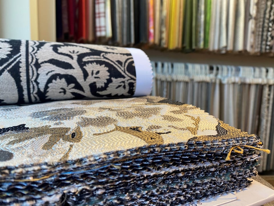 fabric book opened to intricate pattern while a rack of fabric is in the background