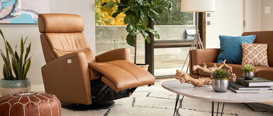 recliner between a plant and coffee table with an ottoman and sofa nearby