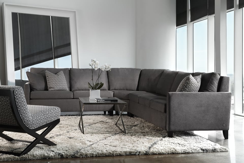 sectional in front of large windows and blank wall, with accent chair and small coffee table over an area rug