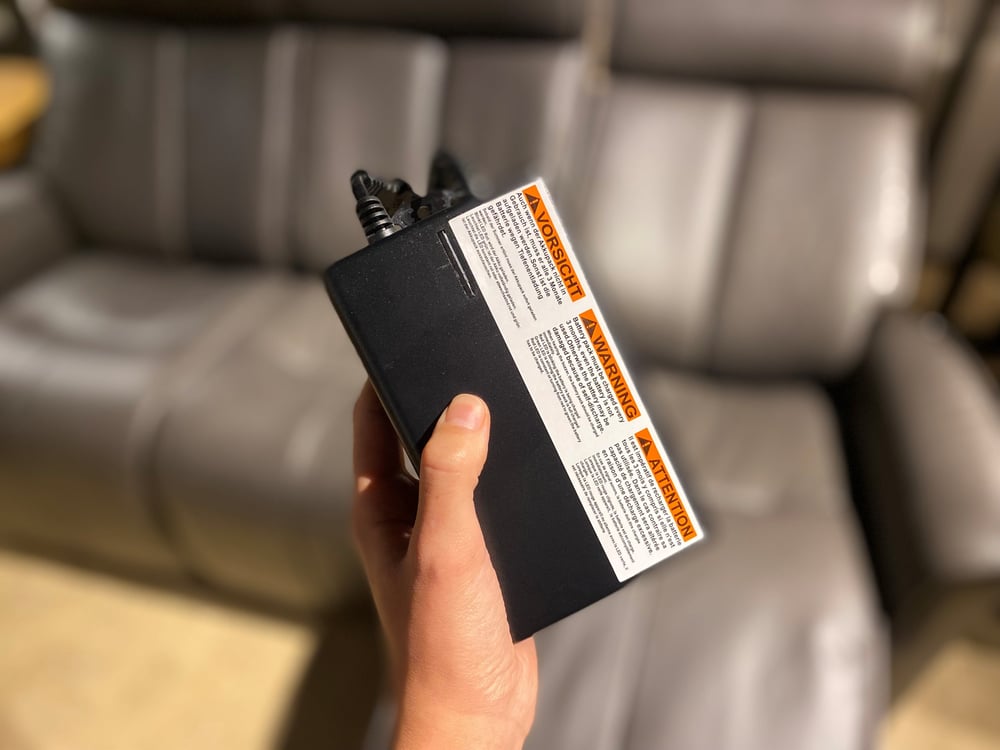 close up of a hand holding a battery pack meant for power reclining furniture with a reclining sofa in the background
