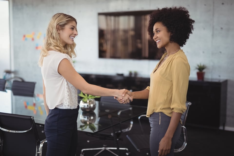 two women happily greet each other with a handshake in a boardroom