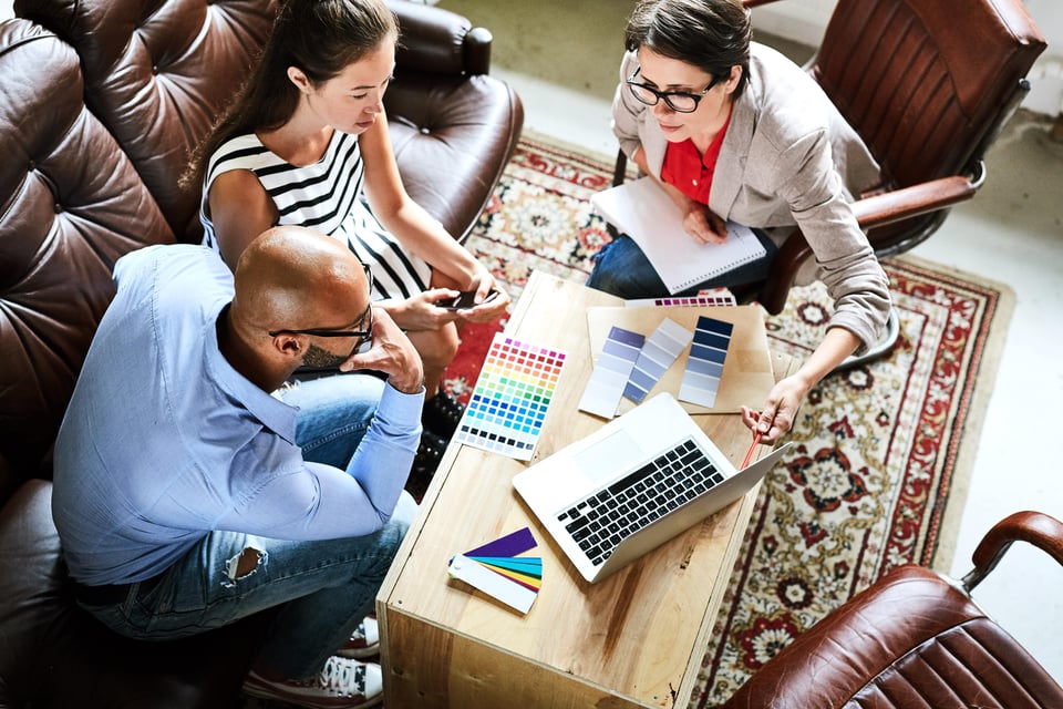 woman designer shows couple information on a laptop while looking at colour swatches on a coffee table