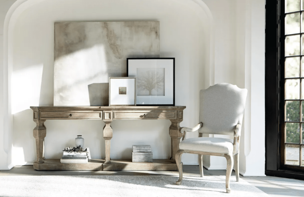 wood console table with three pictures on top and decor on the bottom tier, with an upholstered chair beside