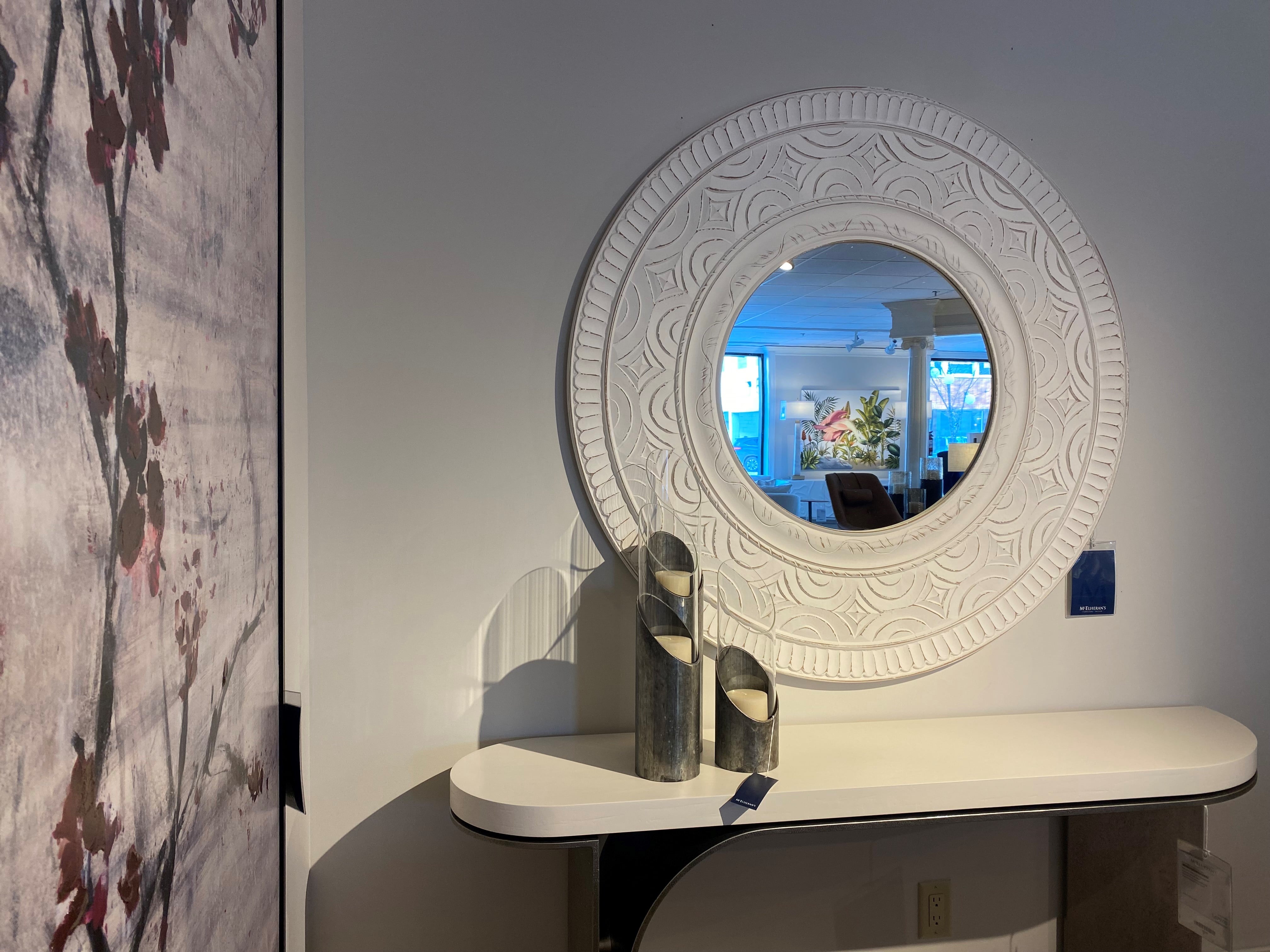 looking at a circular mirror with white frame above a console table holding a three candle set