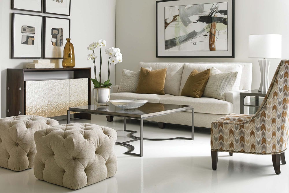 living room setting of a small sofa, accent chair, two ottomans, and a cabinet surrounding a coffee table with art on the walls
