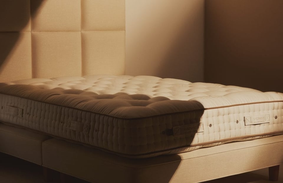undressed Vispring mattress atop a divan and in front of an upholstered headboard