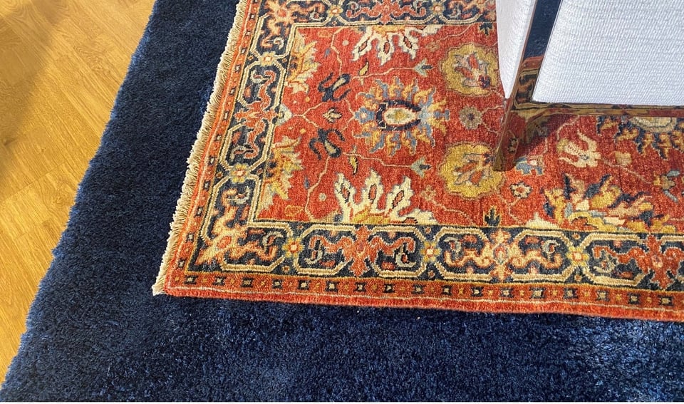intricately designed rug layered over a solid shag rug on a hardwood floor