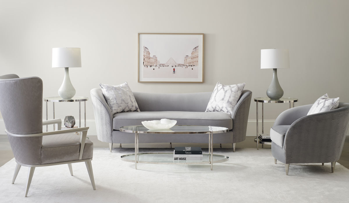 living room setting with a sofa and two accent chairs around a glass oval coffee table and two glass end tables with lamps beside the sofa