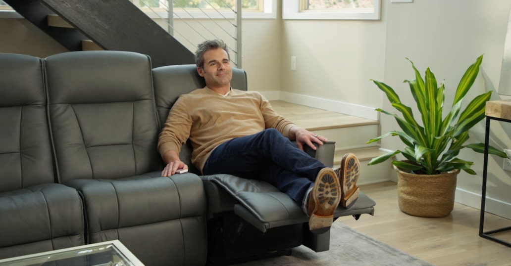 smiling man reclines back in power reclining sofa with a plant nearby