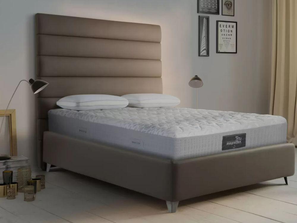 undressed magniflex mattress with two undressed pillows over top in a bed frame with headboard and two surrounding reading lamps